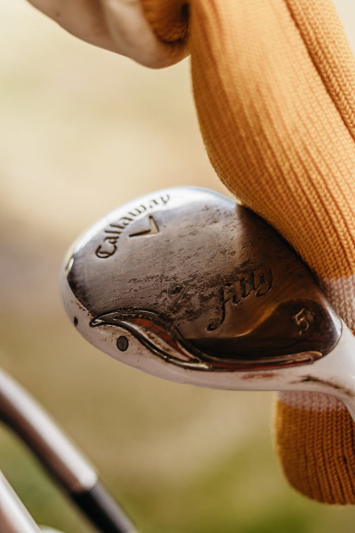 services-img Detailed shot of a steel golf club head being cleaned with an orange glove.
