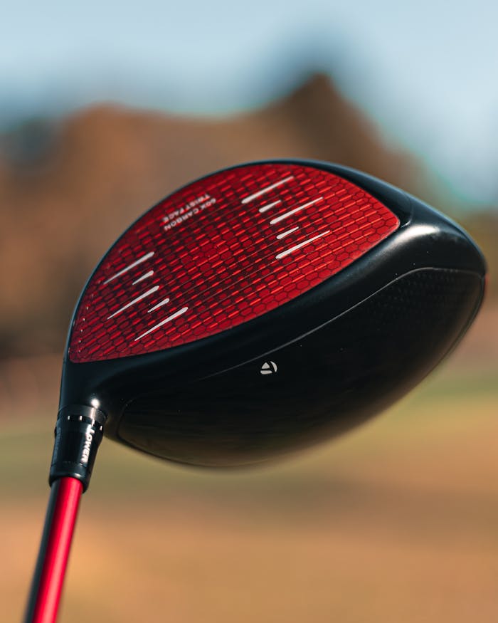 Detailed shot of a red golf club head with blurred background, perfect for sports enthusiasts.