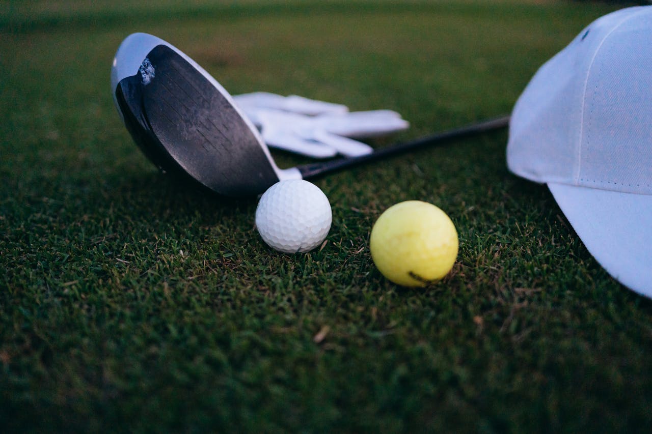 services-01 Close-up shot of a golf club, golf balls, and a cap on grass.